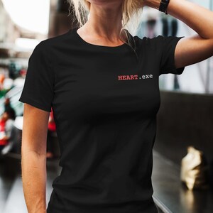 Peut inclure: Un t-shirt noir à manches courtes avec le texte HEART.exe imprimé en rouge et blanc sur la partie supérieure gauche de la poitrine. Le vêtement présente une encolure ronde classique et un ourlet droit, fabriqué en tissu noir uni.