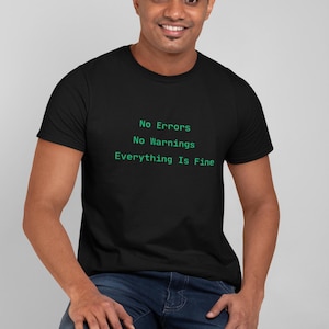 May include: A black short-sleeved t-shirt featuring green text printed on the chest that reads: No Errors, No Warnings, Everything Is Fine. The shirt has a crew neckline and is paired with dark blue denim jeans.