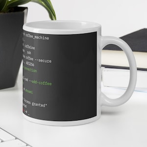 May include: White coffee mug with a black background featuring white and green text that reads "coffee_machine", "caffeine", "ssh", and "access granted". The mug is on a white surface.