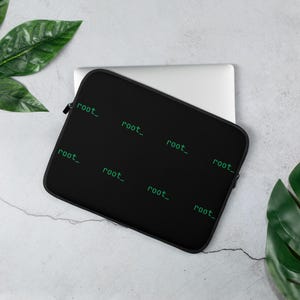 May include: A black laptop sleeve featuring a repeating pattern of the text root_ in a light green monospaced font. The sleeve has a black zipper closure and contains a silver laptop partially visible at the top edge of the protective case.