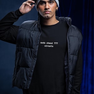 May include: A black sweatshirt featuring the white text "sudo chmod 777 streets" on the chest, worn under a black quilted puffer vest. The outfit includes a light gray beanie topped with white-framed ski goggles with a dark reflective lens.