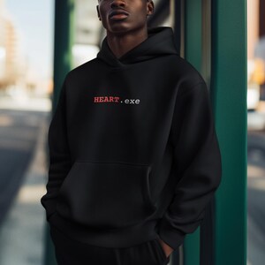 May include: A black hooded sweatshirt featuring a front kangaroo pocket and the text HEART.exe printed on the chest. The word HEART is in red capital letters, while the .exe extension is in white lowercase letters, centered on the upper torso.