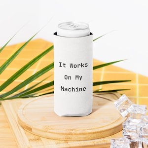 May include: A white can cooler with the text "It Works On My Machine" in black. A silver can is inside the cooler. The cooler is on a wooden cutting board with ice cubes in the foreground.