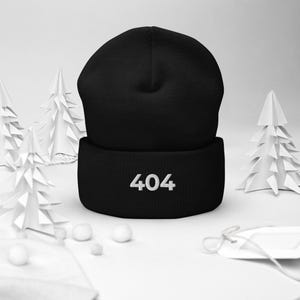 May include: A black beanie with the number "404" embroidered in white on the front. The hat is made of a soft material and is suitable for cold weather. The beanie is displayed on a white surface with decorative paper trees.