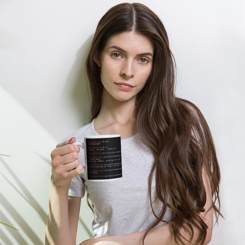 May include: A white ceramic mug featuring a black rectangular graphic printed with white and red computer terminal command line text. The text displays various directory paths and commands including pwd, ls, and git status on a dark background.