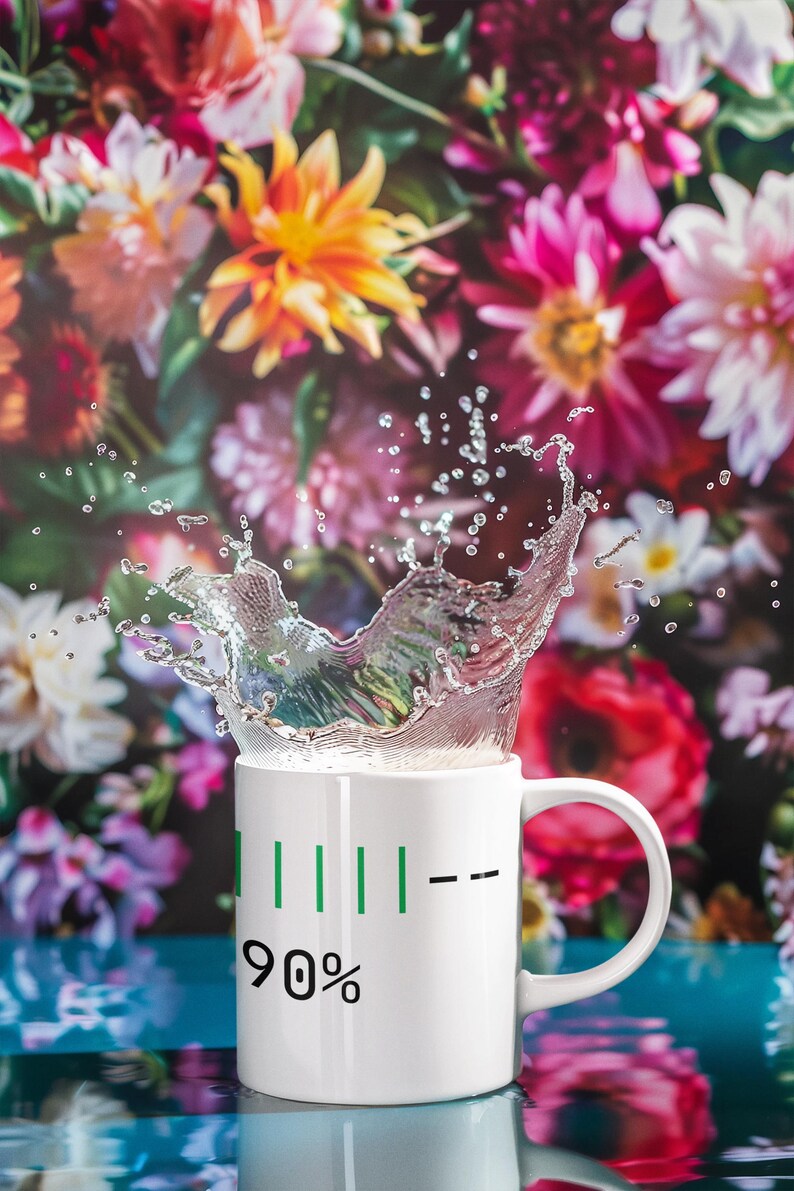 May include: A white ceramic mug with a green battery-like indicator showing 90% capacity. Water is splashing out of the mug. The background features a vibrant floral arrangement with pink, red, and yellow flowers.