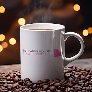 May include: A white ceramic coffee mug with the text "AUTHENTICATION REQUIRED: [INSERT_COFFEE]" and a pink graphic. The mug is filled with coffee and sits on a bed of roasted coffee beans. Steam rises from the coffee.