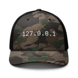 May include: Camouflage trucker hat with a black mesh back and a curved brim. The front panel features a green, brown, and tan camouflage pattern with the white text "127.0.0.1" embroidered on the front.