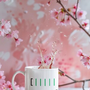 May include: A white ceramic mug with green vertical lines and the number 90, with liquid splashing out. The mug is set against a soft pink background with cherry blossom branches and flowers.