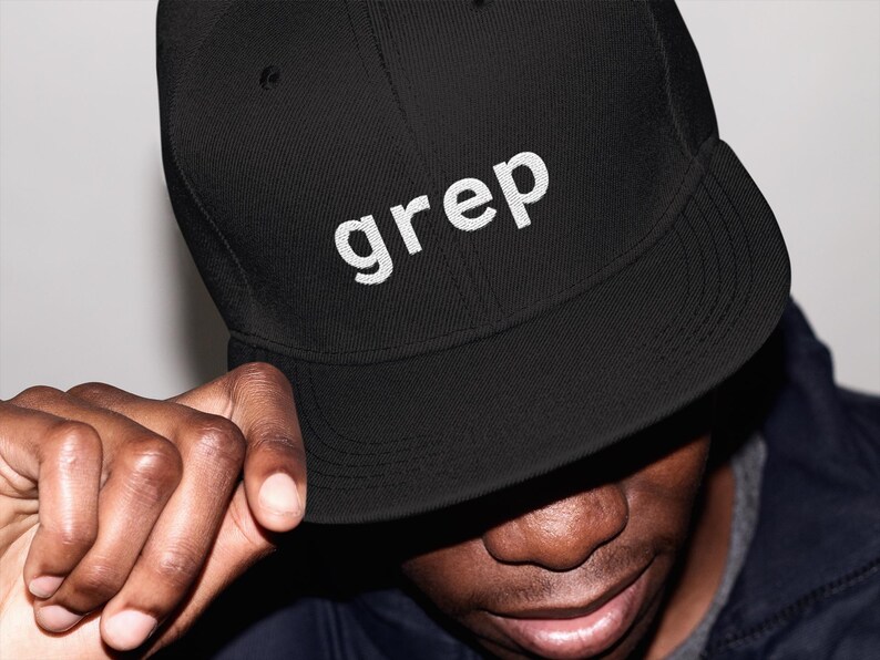 May include: Black baseball cap with the word "grep" embroidered in white. The cap has a curved peak and a structured fit. The person in the image is wearing a dark jacket.