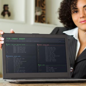 Pu&ograve; includere: Un laptop mostra una "VIM CHEAT SHEET" con comandi e istruzioni. Lo schermo &egrave; nero con testo bianco e verde. Una donna con una giacca nera e una camicia bianca tiene il laptop, sorridendo.