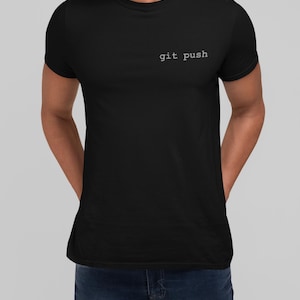 May include: A black short-sleeved t-shirt featuring the text "git push" printed in a white, typewriter-style font on the upper left chest area. The garment has a classic crew neckline and a fitted silhouette, providing a clean and simple look.