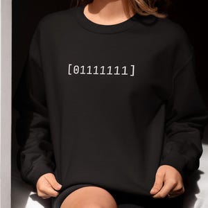 May include: Black sweatshirt with the binary code [011111111] printed in white. The long-sleeved crew neck top is worn by a person. The sweatshirt is a casual style.