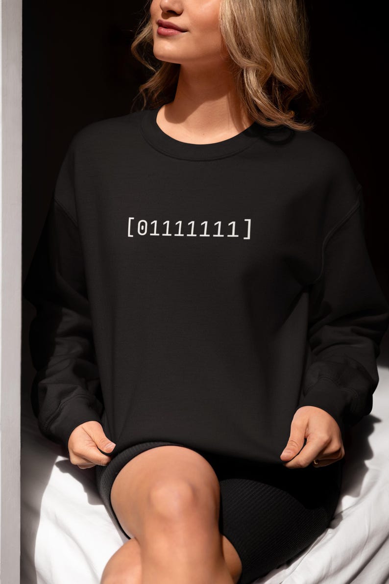 Puede incluir: Una sudadera negra de manga larga con cuello redondo que presenta el texto blanco [01111111] impreso en el centro del pecho. La prenda tiene cuello, pu&ntilde;os y dobladillo acanalados, ofreciendo un ajuste est&aacute;ndar con un acabado de tela negra.