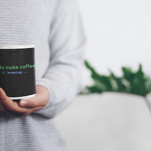May include: A black ceramic mug with a white interior and handle. The exterior features green text that reads "sudo make coffee" followed by blue text on the line below that reads "// brewing..." in a monospaced font style.