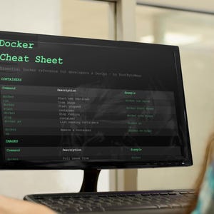 May include: A computer monitor shows a "Docker Cheat Sheet" with green text on a black screen. The text includes commands and descriptions for Docker. The screen is angled towards the viewer, with a keyboard in the foreground. The text includes "CONTAINERS" and "IMAGES".