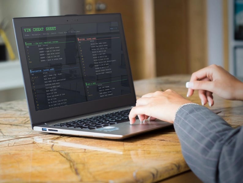 Pu&ograve; includere: Un laptop mostra una "VIM CHEAT SHEET" sullo schermo. Lo schermo mostra righe di codice e comandi in testo verde e bianco. Il laptop &egrave; aperto su un tavolo di legno, con le mani di una persona che digita sulla tastiera.
