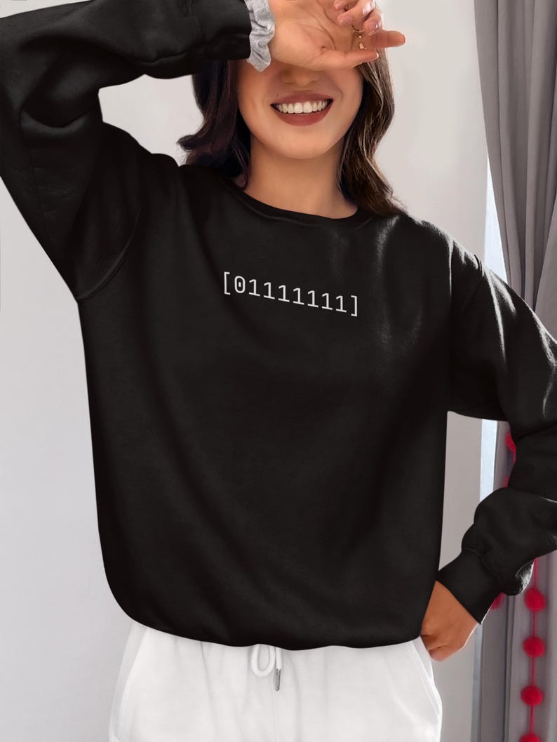 Puede incluir: Una sudadera negra de manga larga con cuello redondo y pu&ntilde;os acanalados. En el centro del pecho aparece el texto blanco [01111111] en una fuente sencilla sin remates. La prenda se combina con una parte inferior de color blanco.