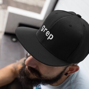 May include: Black baseball cap with a flat brim, featuring the word "grep" embroidered in white. The cap has a structured crown and a flat peak. A classic style, suitable for casual wear.