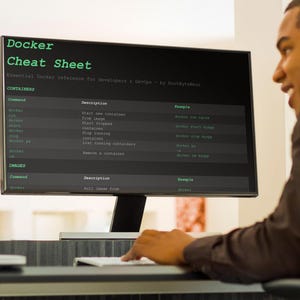 May include: A computer monitor showing a "Docker Cheat Sheet" with commands and descriptions. The screen is black with green text. A person is working at a desk in front of the monitor.