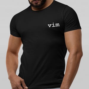 May include: Black crew neck t-shirt with the word "vim" printed in white on the upper left chest. The shirt is made of a soft material and has short sleeves. The model is wearing the shirt.