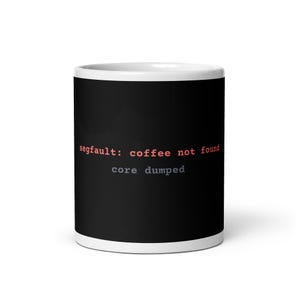 May include: A black ceramic mug with a white interior and rim. The front features the red text "segfault: coffee not found" and the grey text "core dumped" in a monospaced font, mimicking a computer terminal error message on a dark background.