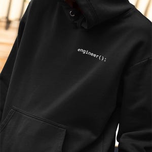 May include: Black hooded sweatshirt with a front pocket and a drawstring hood. The text "engineer();" is printed in white on the upper chest area. The sweatshirt is made of a soft material.