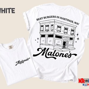 A white t-shirt with a graphic design depicting a building and the text "Malones" written on it.