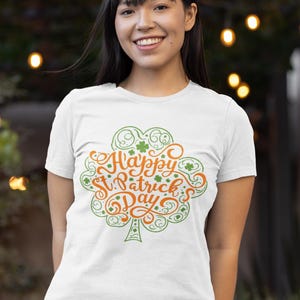 May include: White t-shirt with a green and orange design that says "Happy St. Patrick's Day". The design is in the shape of a shamrock. The person is wearing blue jeans.