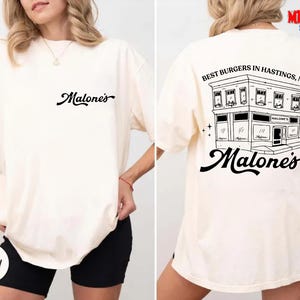 A white t-shirt with a graphic design on the back, depicting a building and the text "Best Burgers in Hastings, MA" printed on it.