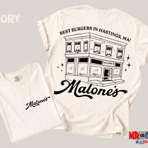 a white t-shirt with a graphic design depicting a building and the text "Malones" written on it.