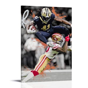 Peut inclure: Impression sur toile représentant une action de football américain. Un joueur en uniforme bleu marine et or saute au-dessus d'un joueur en rouge et or, sur fond noir et blanc avec des éclaboussures orange.