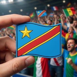 May include: A blue, red, and yellow flag-shaped item, held in a hand, representing the Democratic Republic of the Congo. The flag features a yellow star and a red stripe. In the background, a crowd cheers with flags.