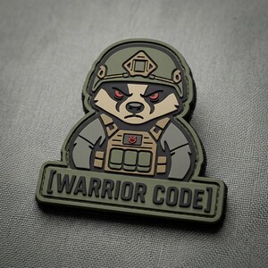 May include: A tactical morale patch featuring a cartoon badger wearing a green combat helmet and tan plate carrier vest. The badger has red eyes and a stern expression. Below the character, a rectangular bar displays the text [WARRIOR CODE].