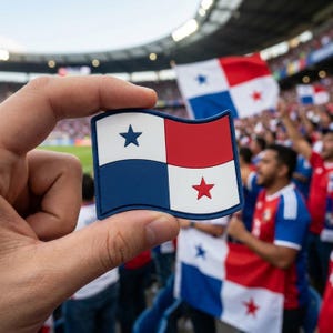 May include: A rectangular patch featuring the Panamanian flag, held in front of a crowd. The flag design includes a white field with a blue star, a red field with a red star, and blue and red quadrants. The patch is held by a person.