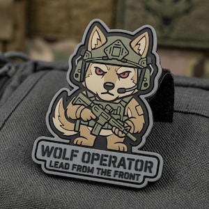 May include: A patch featuring a cartoon wolf wearing a military helmet and holding a rifle. The wolf is tan and brown with red eyes. The patch has the text "WOLF OPERATOR LEAD FROM THE FRONT" in white letters on a gray background.