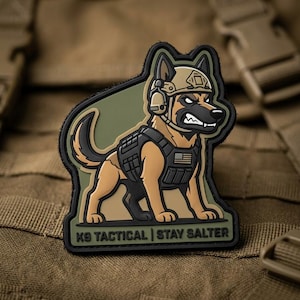 May include: A patch featuring a cartoon German Shepherd dog wearing a tactical vest and helmet. The dog has an angry expression and the patch includes the text "K9 TACTICAL | STAY SALTER" and a small American flag.