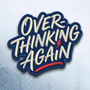 May include: Embroidered patch with the words "OVERTHINKING AGAIN" in white script on a navy blue background. A red lightning bolt and a red line accent the design. The patch has a navy blue border.