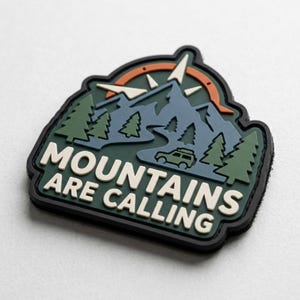 May include: A rubberized patch featuring a dark green background with a blue mountain range, green pine trees, an orange sun arc, and a small green vehicle. The text MOUNTAINS ARE CALLING is embossed in white letters at the bottom of the patch.