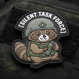 May include: A patch featuring a cartoon raccoon wearing a helmet and vest, holding a grenade. The patch has the text "SILENT TASK FORCE" in a curved banner above the raccoon. The patch is black, brown, green, and gray.