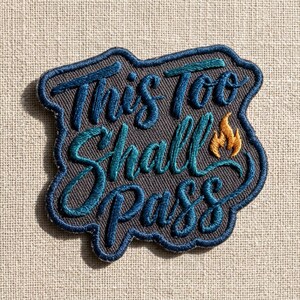 May include: Embroidered patch with the phrase "This Too Shall Pass" in teal and blue script. The patch has a dark gray background with a blue border and a small orange flame detail.