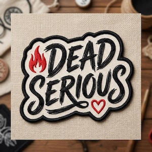 May include: Embroidered patch with the words "DEAD SERIOUS" in black script, outlined in black, with a red flame and heart. The patch is on a beige fabric background.