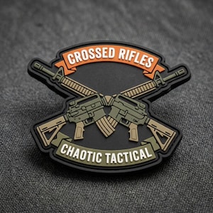 May include: A black patch featuring two crossed rifles in olive green and tan, with the text "CROSSED RIFLES" in orange and "CHAOTIC TACTICAL" in white.
