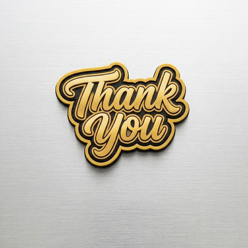 May include: A gold-colored "Thank You" emblem with a black outline. The text is in a cursive font, and the emblem is set against a brushed metal background.
