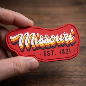 May include: A red rectangular patch with the word "Missouri" in a retro font, featuring white, yellow, and orange accents. The text "EST. 1821" is below. The patch is a souvenir or collectible item.