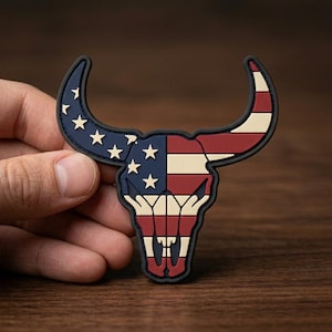 May include: A black-bordered patch in the shape of a bull skull, featuring the American flag design. The horns are blue with white stars, and the skull is red and white striped.