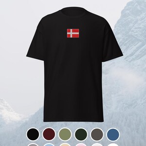 Könnte beinhalten: Schwarzes T-Shirt mit einer kleinen, aufgestickten dänischen Flagge auf der Brust. Die Flagge zeigt ein weißes skandinavisches Kreuz auf rotem Grund. Eine Farbpalette möglicher T-Shirt-Farben wird darunter angezeigt.