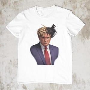 May include: White t-shirt featuring a portrait of a man with dreadlocks, wearing a blue suit and red tie. The image is a humorous parody, blending unexpected elements for a unique design.