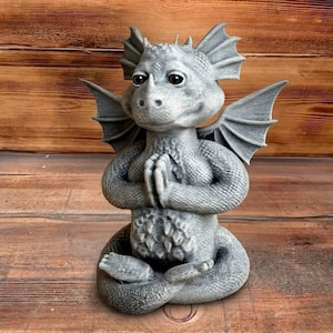 May include: A grey dragon statue in a seated pose, with hands clasped together as if in prayer. The dragon has large wings and a friendly expression, made from a stone-like material. This statue is a decorative garden ornament.