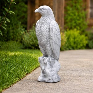 Könnte beinhalten: Eine hellgraue Steinstatue eines Adlers, der auf einem strukturierten Felsensockel steht. Der Adler ist im Profil dargestellt, mit detailliertem Gefieder, einem scharfen Schnabel und Krallen, die sich in die Felsenoberfläche krallen.
